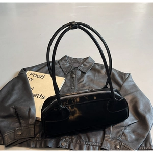 Close-up of glossy black Boston shoulder bag resting on a leather jacket with book