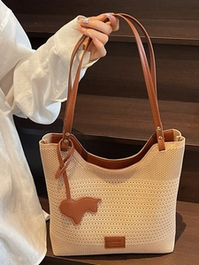 Beige knit tote bag with brown leather straps and bull charm on a wooden staircase