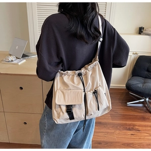 Detail view of large nylon crossbody bag featuring double front pockets and drawstring closure