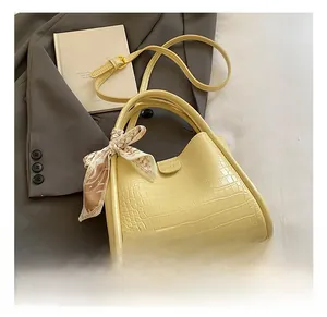Détail du sac seau jaune gaufré crocodile avec poignée en foulard sur un blazer