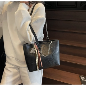 Detail of black leather tote bag with metallic chain and tennis racket pendant accessory