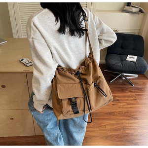 Detail view of large nylon shoulder bag featuring dual front pockets and drawstring closure