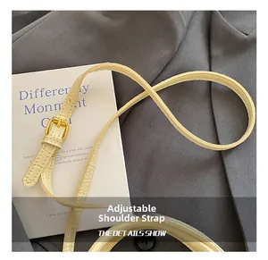 Détail de la bandoulière réglable en cuir de crocodile beige avec boucle dorée sur un sac