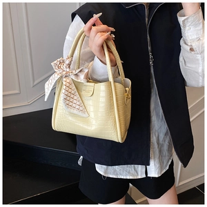 Gros plan d'un sac à main jaune pâle à texture crocodile orné d'un foulard en soie chic