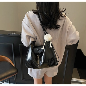 Detail view of black glossy leather hobo bag featuring a white plush keychain and front pocket