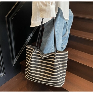 Close-up of large striped woven tote bag with black handles on wooden stairs