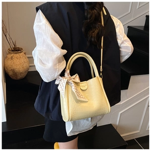 Détail d'un sac seau jaune clair motif crocodile avec foulard en soie et plaque logo