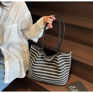 Close-up of black and white striped woven tote bag with slim black handles in a casual setting
