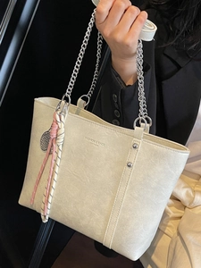Minimalist beige leather tote bag with silver chain handles and woven tassel charm