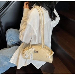 Détail du sac bandoulière en cuir jaune crème avec breloque cœur perlé et nœud en dentelle