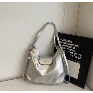 Detail of silver metallic tote bag with white plush ball charm and magnetic flap closure