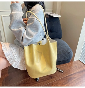 Detail view of bright yellow tote bag with crocodile texture and long shoulder strap