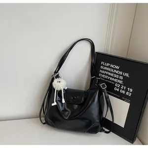 Detail of black glossy leather tote bag featuring a cute white plush monster charm