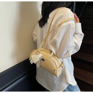 Détail d'un sac en cuir verni crème avec nœud en dentelle et pendentif cœur en perles