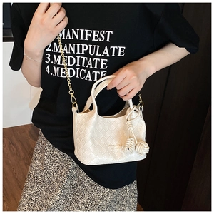 Détail d'un sac seau tressé blanc avec texture cuir, chaîne dorée et breloques boules