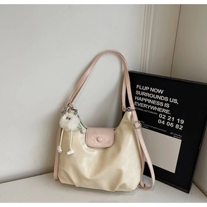 Detail view of beige shoulder tote bag with light pink strap and white fur ball charm