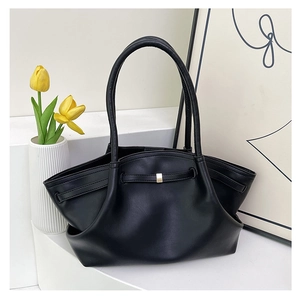 Detail of a black minimalist tote bag with folded wings and gold metal hardware