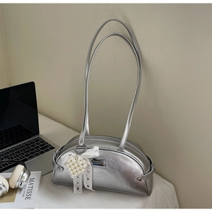 Détail du sac argenté plissé avec un nœud en dentelle et un pendentif cœur perlé