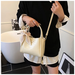 Détail d'un sac seau beige en cuir embossé croco avec un foulard en soie à carreaux