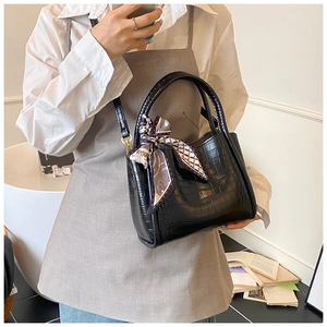 Détail de la texture cuir croco noir avec un élégant foulard décoratif en soie sur le sac