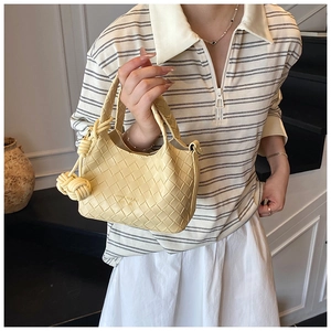 Détail d'un sac seau en cuir tressé jaune avec logo de la marque et breloque en nœud