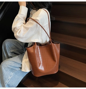 Brown crocodile pattern bucket bag with slim straps worn by a model on wooden steps