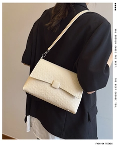 Detail of a textured cream shoulder bag featuring an elegant flap and slim strap