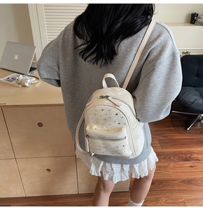 Détail d'un petit sac à dos crème avec strass argentés porté par un mannequin en intérieur