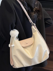 Minimalist cream hobo bag with pink flap and plush ball accessory worn by a model