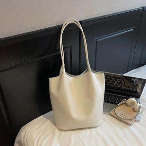 Close-up of off-white crocodile embossed tote bag with slim shoulder straps on a white bed