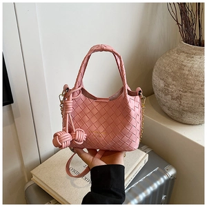 Détail du sac seau en cuir tressé rose avec pompon assorti et bandoulière chaîne
