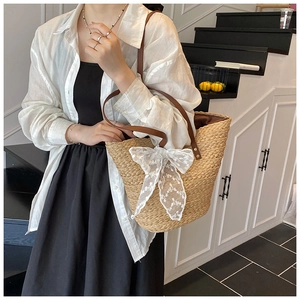 Detail einer handgeflochtenen Strohtasche mit weißer Spitzenschleife und Ledergriffen