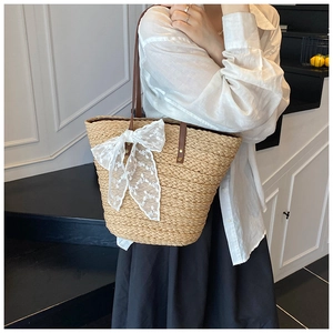 Detail der handgewebten Strohtasche mit Spitzenschleife und Ledergriffen am Model