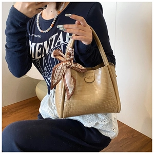 Détail du sac seau beige à motif crocodile avec ruban décoratif et boucle métallique chic