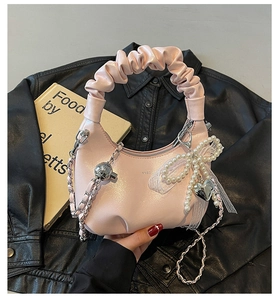 Close-up of pink pleated handbag with pearl bow charm and silver chain strap