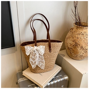 Detail der handgewebten Strohtasche mit weißer Spitzenschleife und braunem Gurt