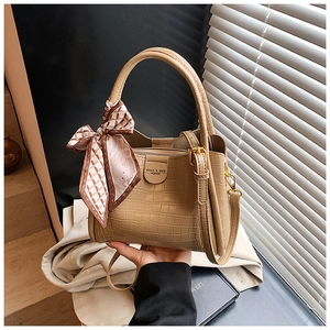 Détail d'un sac beige motif crocodile avec nœud en soie et logo de la marque