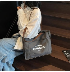 Close-up of grey canvas tote bag with brown handles and coherent design letter printing
