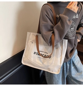 Close-up detail of white canvas tote bag with letter print and brown shoulder strap