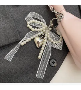 Detail of pearl bow charm with lace ribbon and heart pendant on a pink leather bag