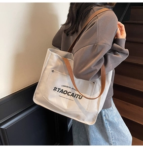 Detail of canvas tote bag with metal buckle pocket and branded lettering on a shoulder strap