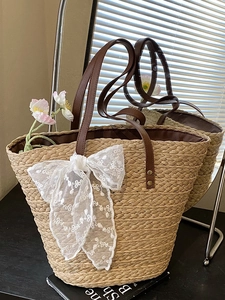 Strohtasche mit braunen Ledergriffen und weißer Spitzenschleife für den Strandurlaub