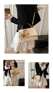 Detail view of ivory white crossbody bag with polished metal lock and cute bear charm