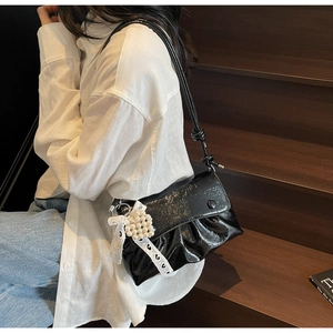 Détail d'un sac à bandoulière noir brillant plissé avec breloque cœur perle et dentelle