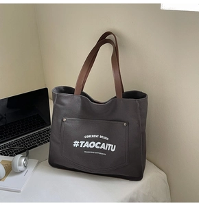 Detail view of charcoal canvas tote bag with leather strap and laptop on white table