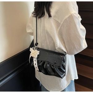 Détail du sac en cuir verni noir avec plis et accessoire de charme en perles