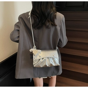 Détail du sac bandoulière argenté plissé avec nœud en perles et boutons décoratifs