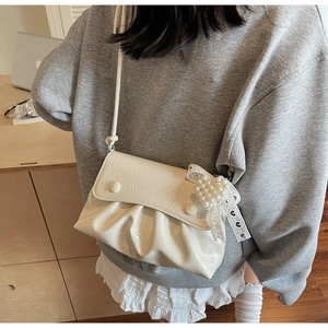 Gros plan d'un sac crème plissé avec breloque cœur perlé et ruban de dentelle chic