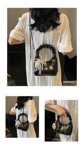 Detail of black pleated handle handbag with pearl lace bow charm and metal chain strap