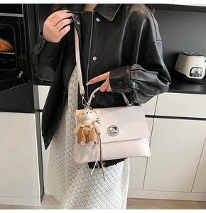Detailed shot of a white faux leather crossbody bag with silver lock and bear charm